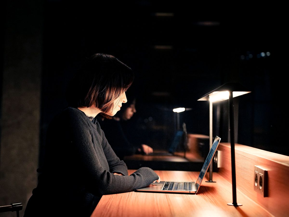A podcaster working alone late at night, editing on a laptop.
