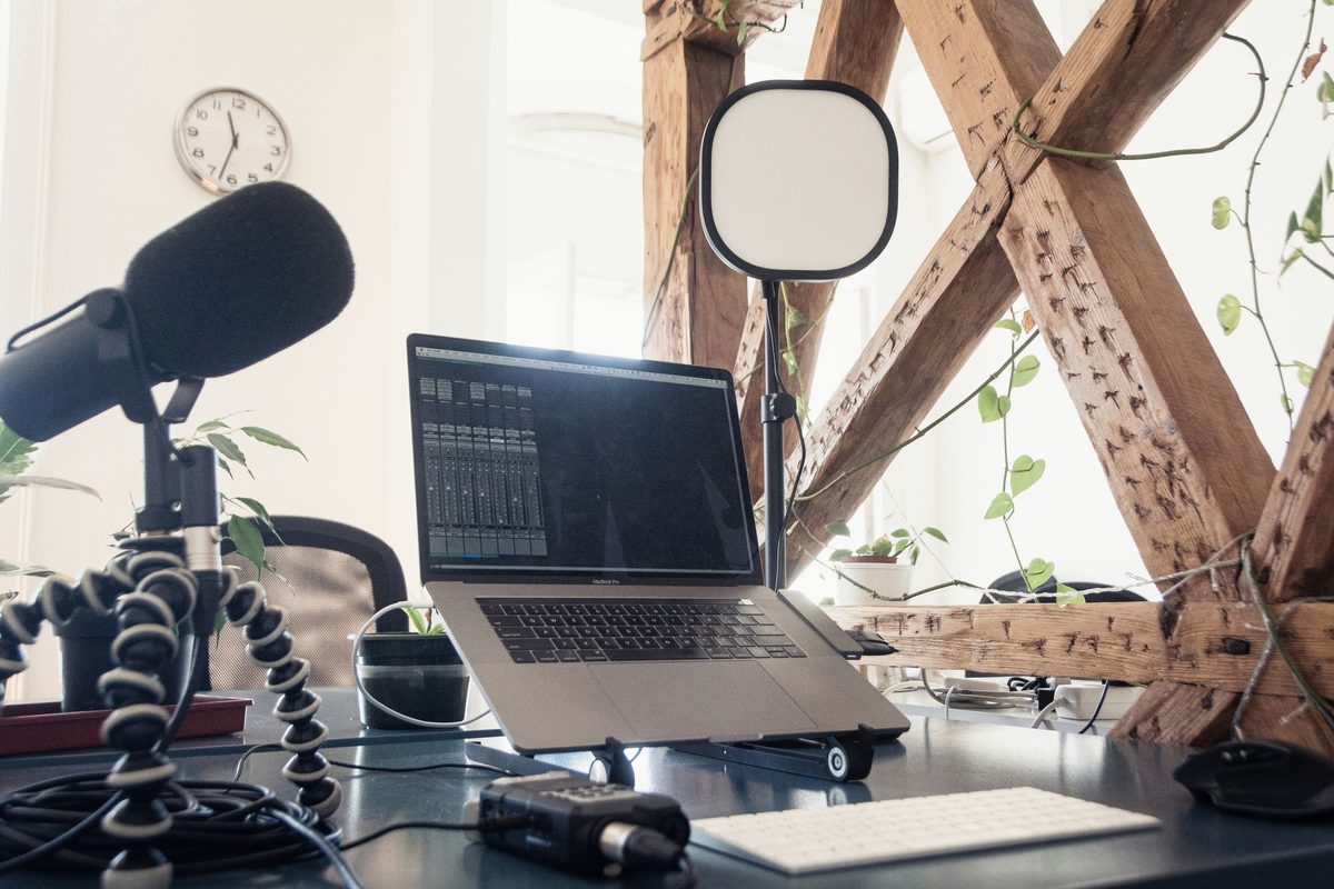 A podcast microphone and laptop set up on a bright desk.